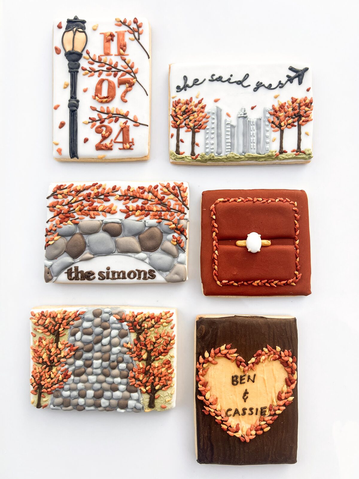 Autumn-themed engagement cookie set in rust and orange with a stone bridge, ring box, and 'Ben & Cassie' heart design
