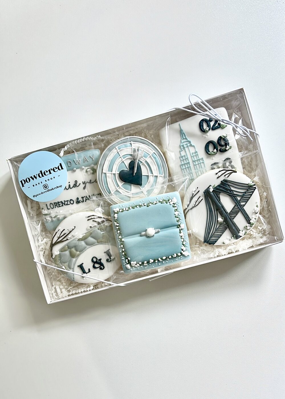 Custom engagement cookie gift box with 'Lorenzo & Janice' script, ring box, and city skyline designs